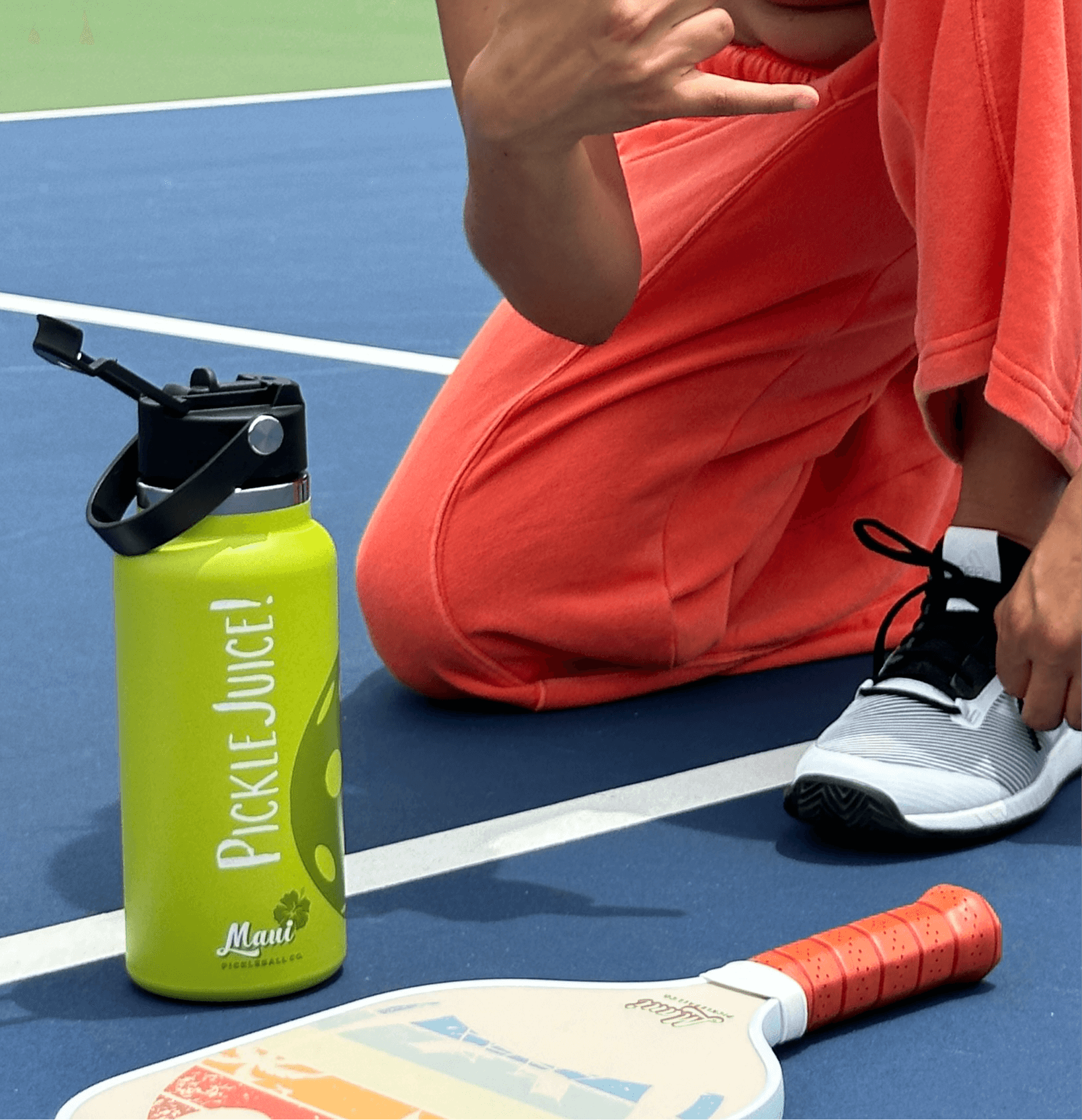 green stainless steel water bottle and a rainbow pickleball paddle on a court