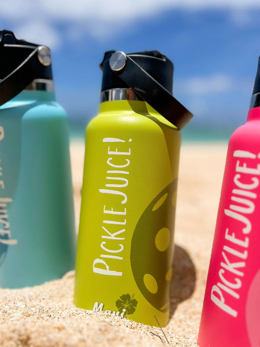 green pickleball water bottle on the beach with a pink bottle and a teal blue bottle