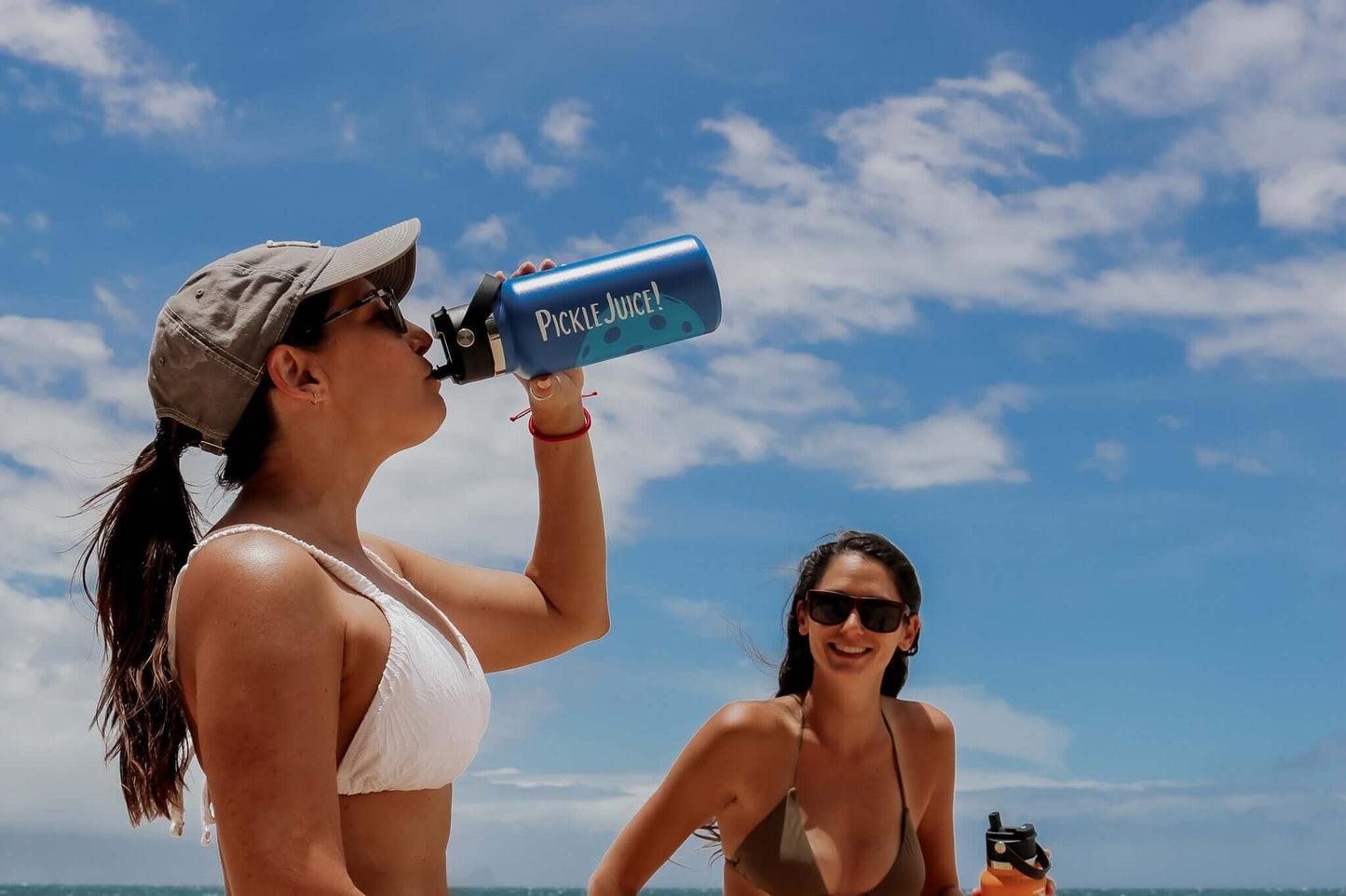 2 woman on the beach laughing and drinking from a funny pickleball water bottle